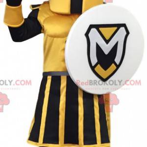 Gelbes und schwarzes Kriegermaskottchen mit einem Schild. -