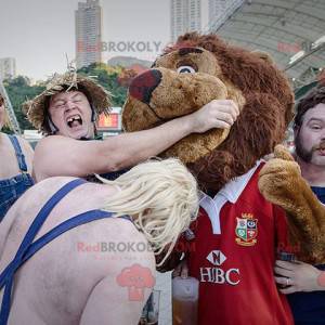 Braunes Löwenmaskottchen ganz haarig in roter Sportbekleidung -